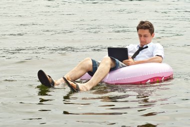 Pembe şişme dairede tişörtlü bir adam. Dizüstü bilgisayarı olan adam nehirde yüzüyor. Tatil, taşeronluk ve serbest çalışma kavramı. İş adamının yanında metin ve kopyalama alanı.