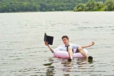 Pembe şişme dairede tişörtlü bir adam. Dizüstü bilgisayarı olan adam nehirde yüzüyor. Tatil, taşeronluk ve serbest çalışma kavramı. İş adamının yanında metin ve kopyalama alanı.