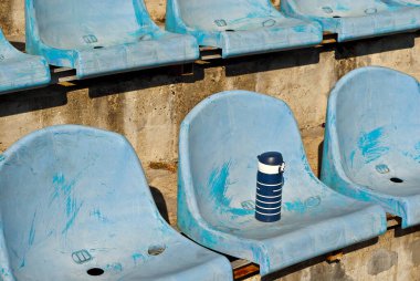Stadyumda bir sürü boş koltuk var. Koltukta su şişesi var. Sporcular için iç. Plastik koltuklar sıraya dizildi. Kirli ve tırmalanmış hayran koltukları.