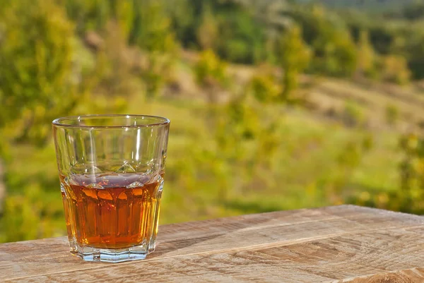 Glass with drink on a background of greenery and nature. Whiskey on an old wooden board. Sunny summer day. Mockup for design. Copy space and place for products.