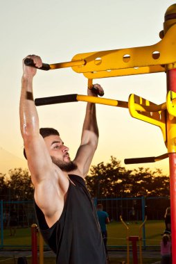 Bir adam gün batımının arka planında sarı bir kavşağa yanaşıyor. Sakallı bir sporcuya turuncu güneş ışığı. Adam terden sırılsıklam. Arka planda şehir stadyumu ve halk spor sahası.