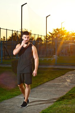 Çocuk parkında koşan bir adam. Günbatımı arka planında bir sporcu. Adam antrenman sırasında yemek yiyor..