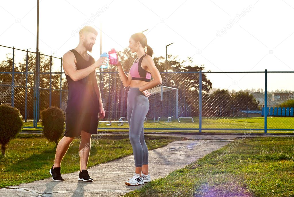 Couple running in the park. Athletes train together. Man and woman with bottles in their hands.