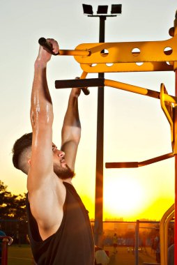 Bir adam gün batımının arka planında sarı bir kavşağa yanaşıyor. Sakallı bir sporcuya turuncu güneş ışığı. Adam terden sırılsıklam. Arka planda şehir stadyumu ve halk spor sahası.