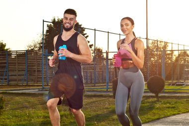 Parkta koşan bir çift. Sporcular birlikte antrenman yapar. Ellerinde şişeler olan kadın ve erkek..