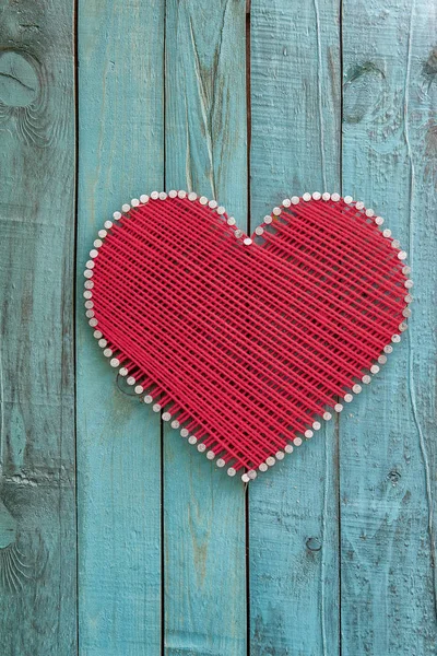 Decorative heart of threads fixed on nails on a wooden blue background.