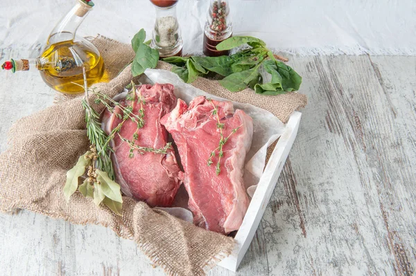 Cuts of beef for grilling on a wooden cutting Board with spinach, rosemary and Provencal herbs for the marinade in a rustic style. Copy spase
