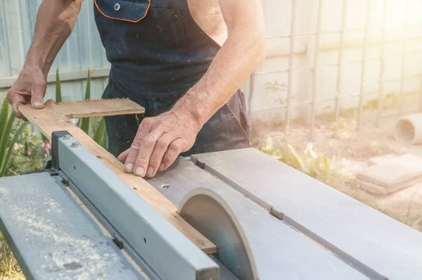 The master sharpens the wooden panel with an electric sander on a Sunny day in the garden. Close up.