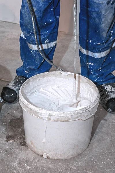 Electric mixer mixes paint in a white bucket. Paddle mixer over a bucket of white paint for the wall, tools and accessories for DIY, close-up workflow.