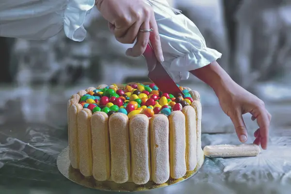 Female hands cut a cake with a lot of colored round chocolates at a children\'s party.