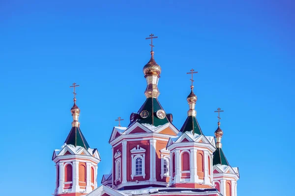 Golden domes with golden crosses over a monastery in Russia against a blue clear sky.