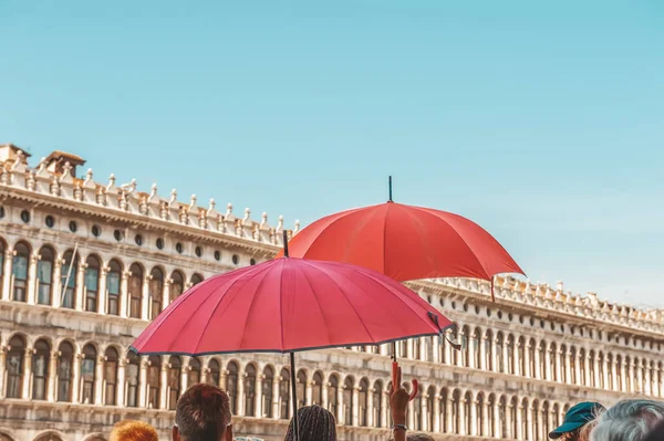 Red umbrellas of tour guides conducting tours on the background of the Piazza San Marco in Venice. Tourist destination.