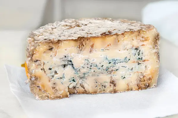 A slice of blue aged delicatessen Stilton cheese on a white table. Farm quality products
