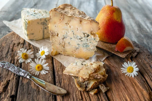 A slice of blue aged Stilton cheese on a wooden table. Cheese is served with a beautiful ripe pear. The quality of farmers \' agricultural products. Delicious English cheeses from Russian farmers