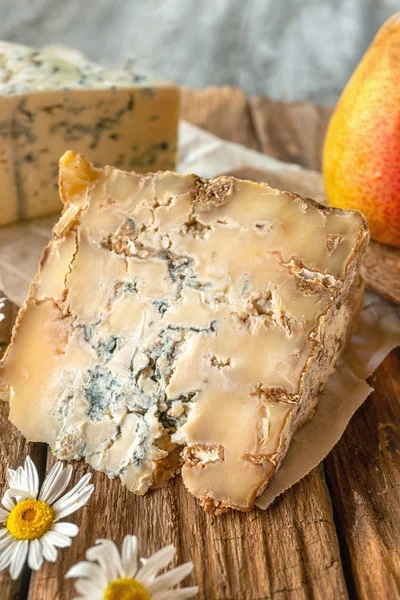 A slice of blue aged Stilton cheese on a wooden table. Cheese is served with a beautiful ripe pear. The quality of farmers ' agricultural products. Delicious English cheeses from Russian farmers