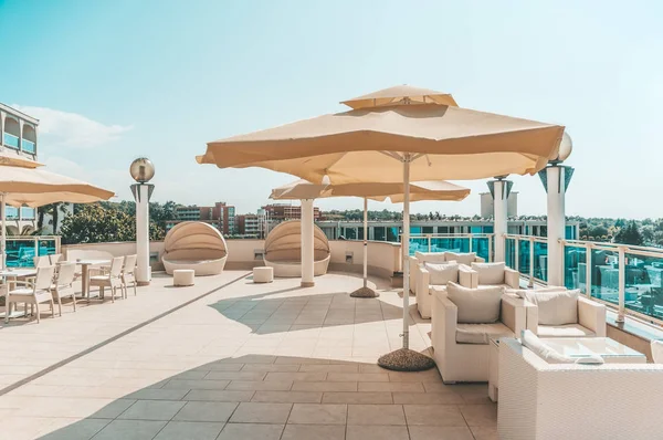 Large white umbrella and outdoor furniture sofas and rattan chairs with cushions and a glass-topped table. Place to relax on the terrace of the resort