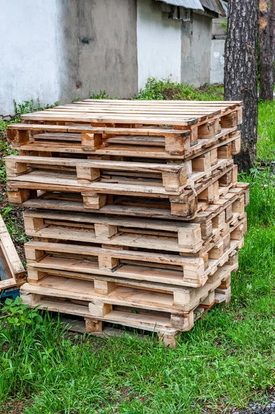 Stacked wooden pallets are stacked on the streets outside the premises. Old pallets at the building on the road