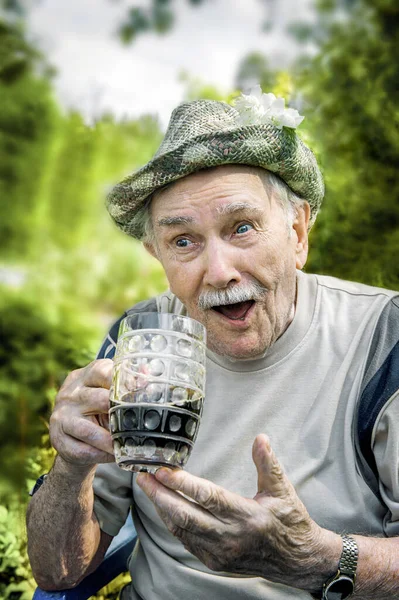 Portrait of a handsome elderly man of 87 years old, drinking a cool drink in the garden after work. Happy active old age. A man drinks dark beer.