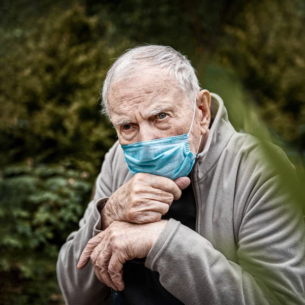 old man in a medical mask in the open air, so as not to get infected with the virus. Prevention of viral diseases. Loneliness of old people.