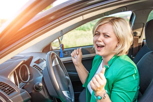 portrait of a young female driver at the wheel. Happy cheerful blonde with blue eyes sings at the wheel of a car.