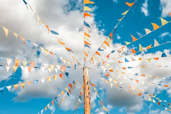 Colorful bright triangular Bunting flags on a blue sky background with white clouds. concept of celebration and fun. Multicolored triangular small flags to celebration party against blue sky as a background.Street holiday concept.