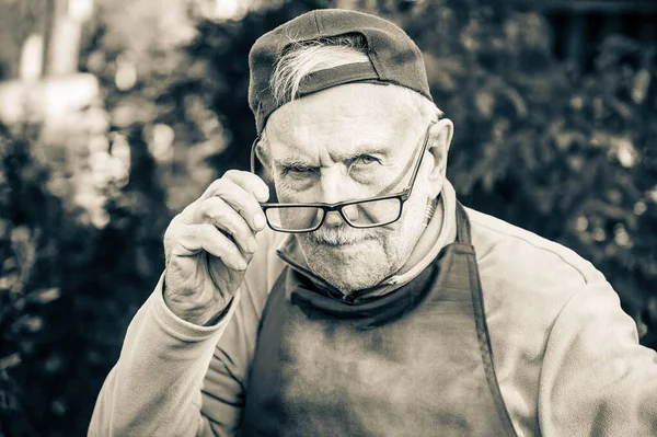 tired old man looks at his interlocutor, adjusts his glasses. The old man can\'t see very well without his glasses. Black and white image.