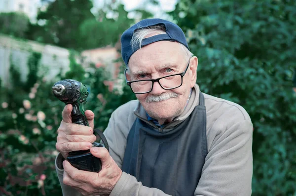 Happy old man posing with an electric drill, smiling. Old farmer with a drill. Copy space