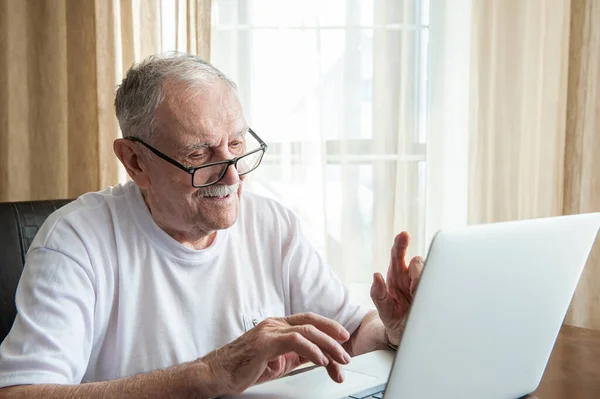 Older man at home in front of a laptop. A gray-haired old man with glasses works at home in front of a laptop. The concept of communication of old people.