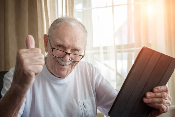 Happy elderly man at home with laptop. A gray-haired old man with glasses is happy and gestures that everything is OK. The concept of communication between older people.