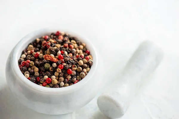 White porcelain mortar and pestle with hot red chili pepper and different types of peppers. Peppers are prepared for grinding and grinding in a stone mortar. Copy space.