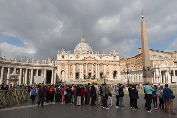 Tourists and main facade of Saint Peter's Basilica at Saint Peter's Square with rainy clouds on background, Vatican city state, Italy.