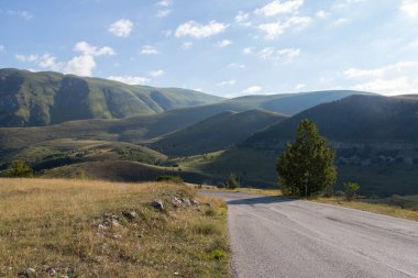 Güneşli bir günde, arka planda dağlarla birlikte asfalt yol manzarası, İtalya.