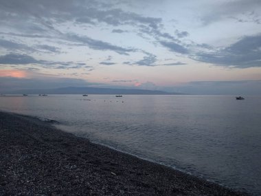 Çakıl taşları, deniz, ufuk çizgisi ve arka planda gün batımı ışığı olan deniz manzarası, Sicilya, İtalya.