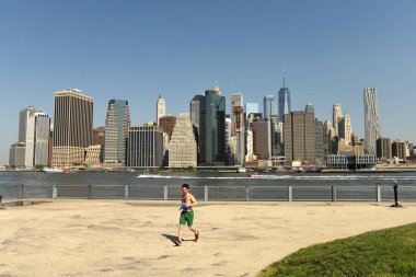 New York, Amerika Birleşik Devletleri - 25 Mayıs 2018: Arka plan, alt Manhattan'ın finans merkezi ile Brooklyn Bridge Park içinde kaçak bir adam.