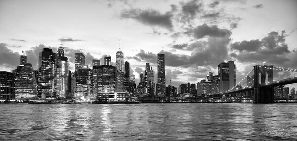 New York City, financial district in lower Manhattan with Brooklin Bridge at night, USA. BW
