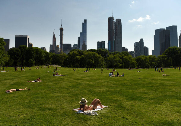 New York, USA - May 25, 2018: People relax on Sheep Meadow in Central Park and skyscrapers of the Manhattan at the background.