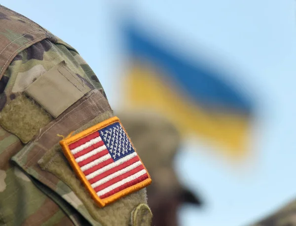 American Flag on Soldiers arm and flag of the Ukraine at background. US military help to Ukraine.