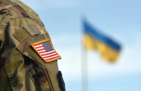 Bendera Amerika di lengan tentara dan bendera Ukraina di latar belakang. Bantuan militer AS untuk Ukraina . — Stok Foto