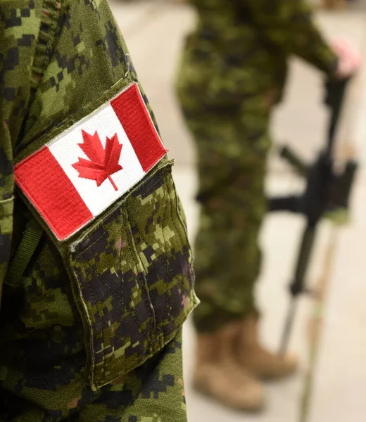 Flag of Canada on the military uniform and soldier with weapon on the background. Canadian soldiers. Canadian Army. Remembrance Day. Canada Day.