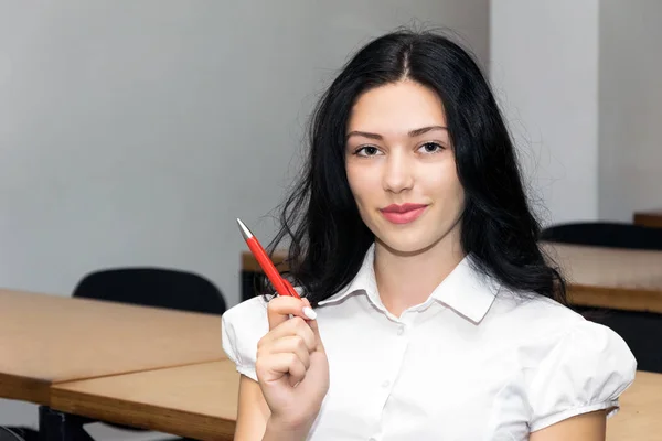 Menina sorridente bonito com caneta, sentado em sala de aula. Educação foto conceito — Fotografia de Stock