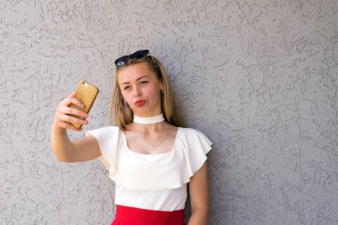 Bel-up ile hassas şekil ve güzel düz sarı saçlar gorgeously giyimli genç kadın portresi. Modern smartphone cep telefonu ile güzel sarışın alarak selfie. Grey ile kopya alanı sağ tarafında izole