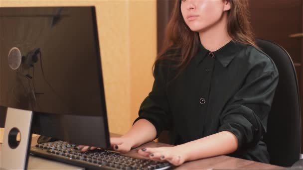 Uma senhora gira a trabalhar no computador no escritório. Uma menina com pregos pretos em um vestido preto está digitando texto em um teclado preto e olhando para o monitor . — Vídeo de Stock