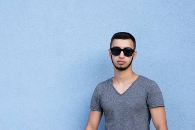 Bel, dikey, kendinden emin yakışıklı esmer adamın resim için poz. Güçlü çekici adam şık gözlük takıyorum. Alanı solundan kopyalayın. Üzerinde mavi arka plan izole