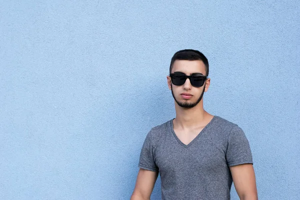 Bel, dikey, kendinden emin yakışıklı esmer adamın resim için poz. Güçlü çekici adam şık gözlük takıyorum. Alanı solundan kopyalayın. Üzerinde mavi arka plan izole