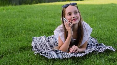 Smartphone kullanarak yazlık elbise genç kız güzel Park, çimenlerin üzerinde yatıyor.