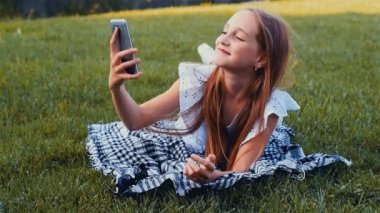 Hareket eden telefon ile çim üzerinde yalan selfie portre yeşil park, smartphone kullanarak yapma genç güzel kız. Dereceli renk