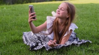 Hareket eden telefon ile çim üzerinde yalan selfie portre yeşil park, smartphone kullanarak yapma genç güzel kız