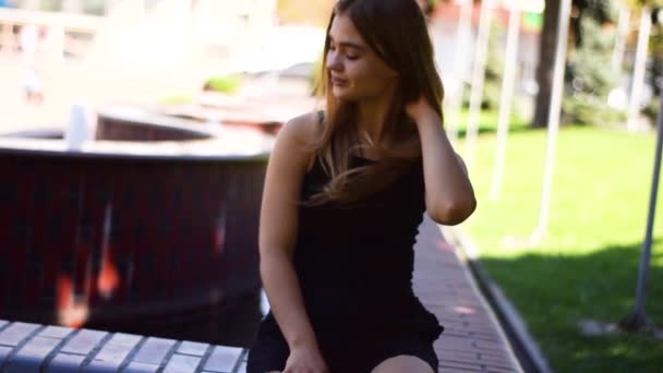 Mujer rubia joven sentada en un banco y sonriendo — Vídeo de stock