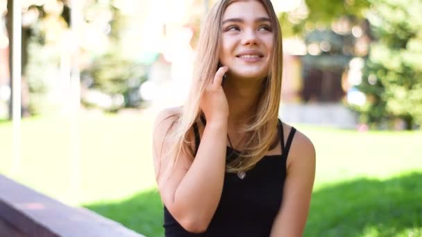 Vista de cerca de una atractiva joven rubia en una brillante luz del atardecer usando el teléfono . — Vídeo de stock