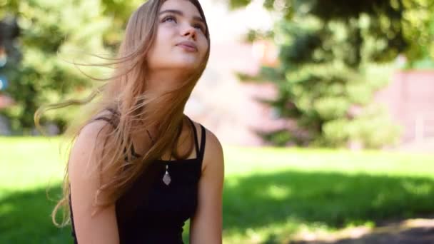 Preciosa adolescente con el pelo largo y recto rubia sentada en el parque — Vídeo de stock